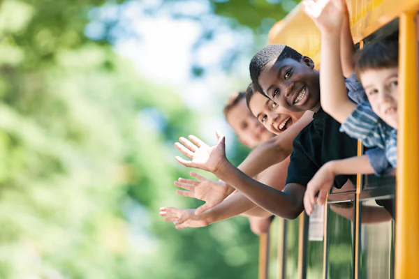 Elementary aged kids smiling and waving while hanging out the windows of a school bus