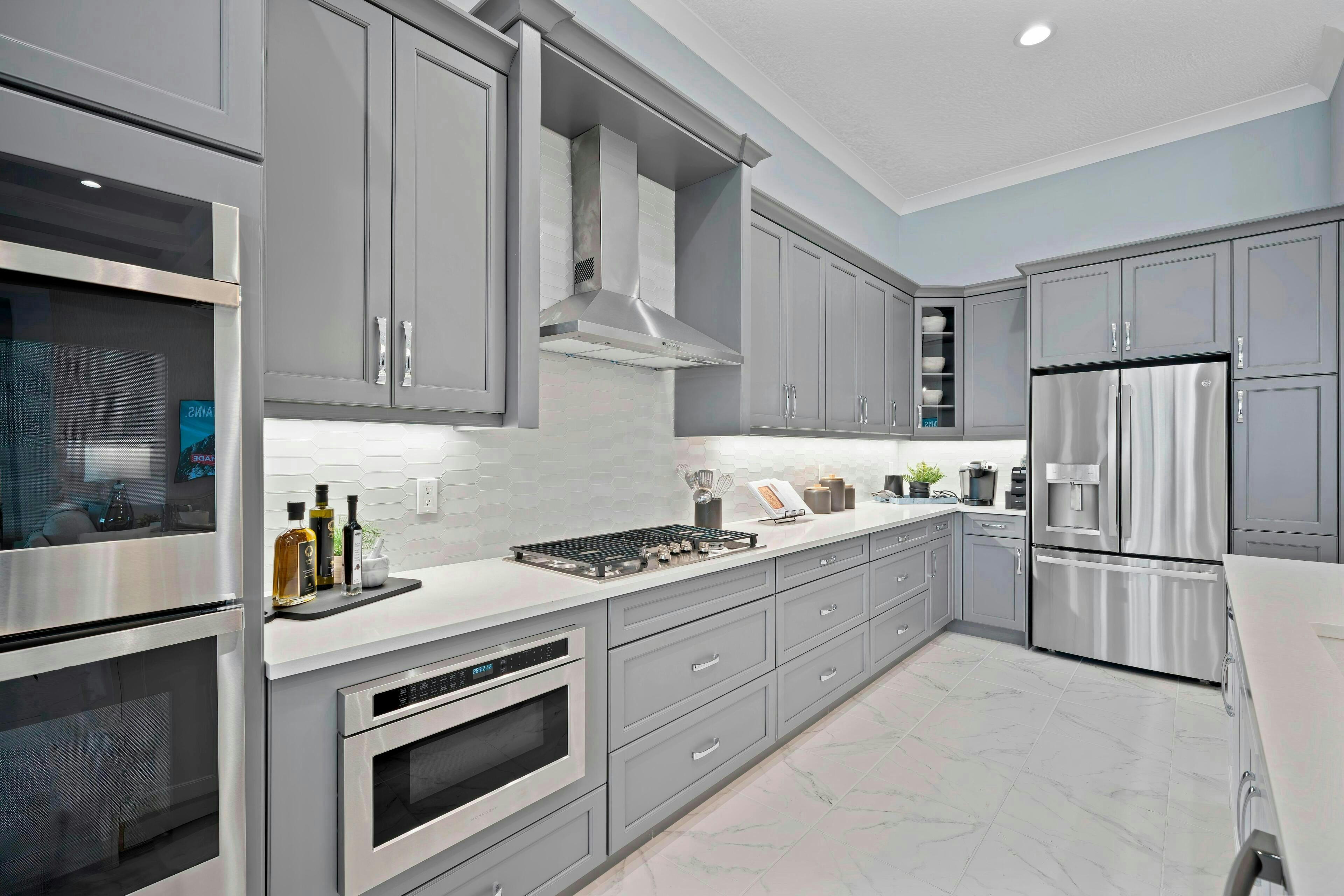 Cook wall in kitchen with grey cabinets, grey tile backsplash and stainless steel appliances