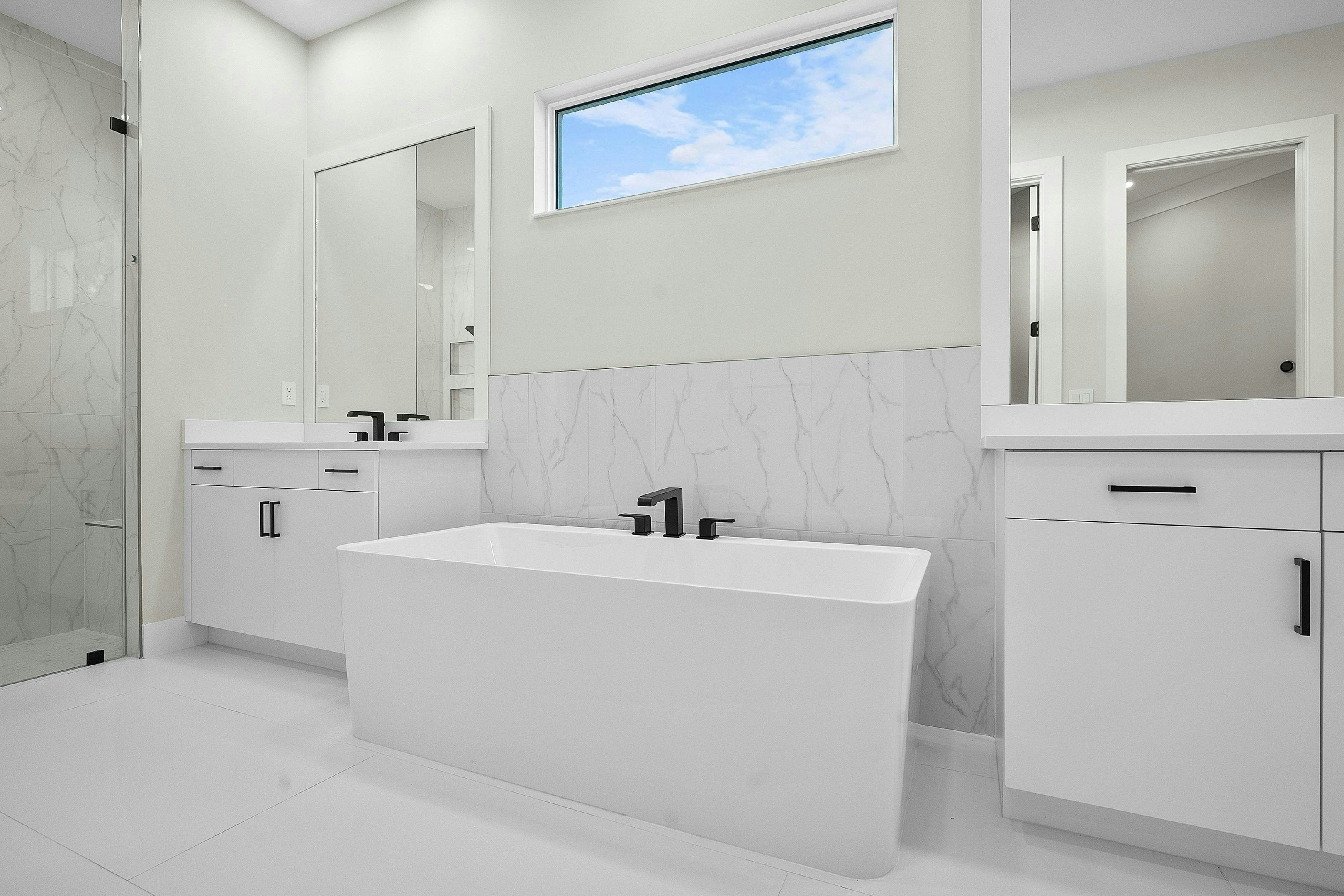 Master bath with modern rectangular soaking tub, split vanity and matte flooring all white