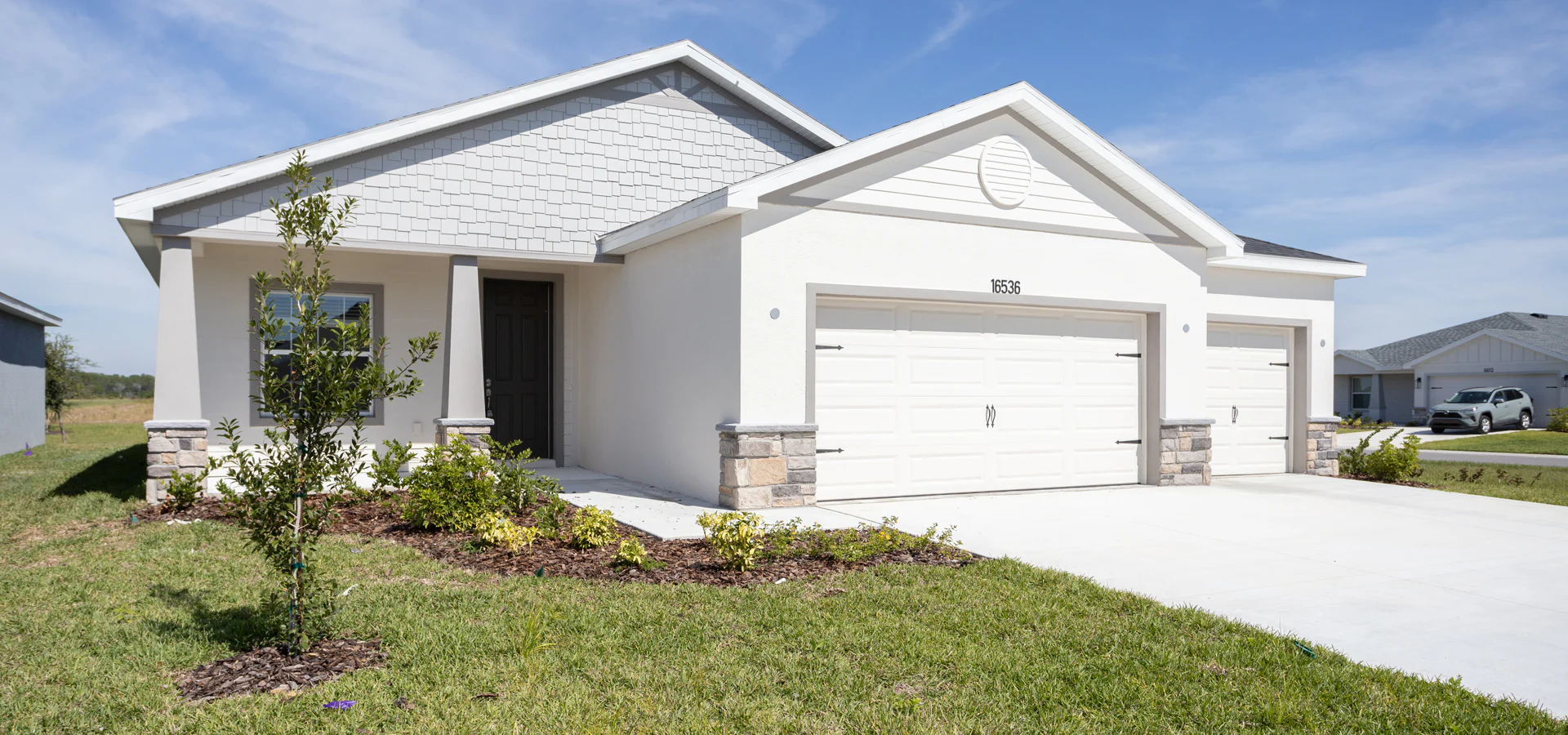 Exterior of the Summerlyn II by Highland Homes, featuring a front porch, 3-car garage, and stone accents