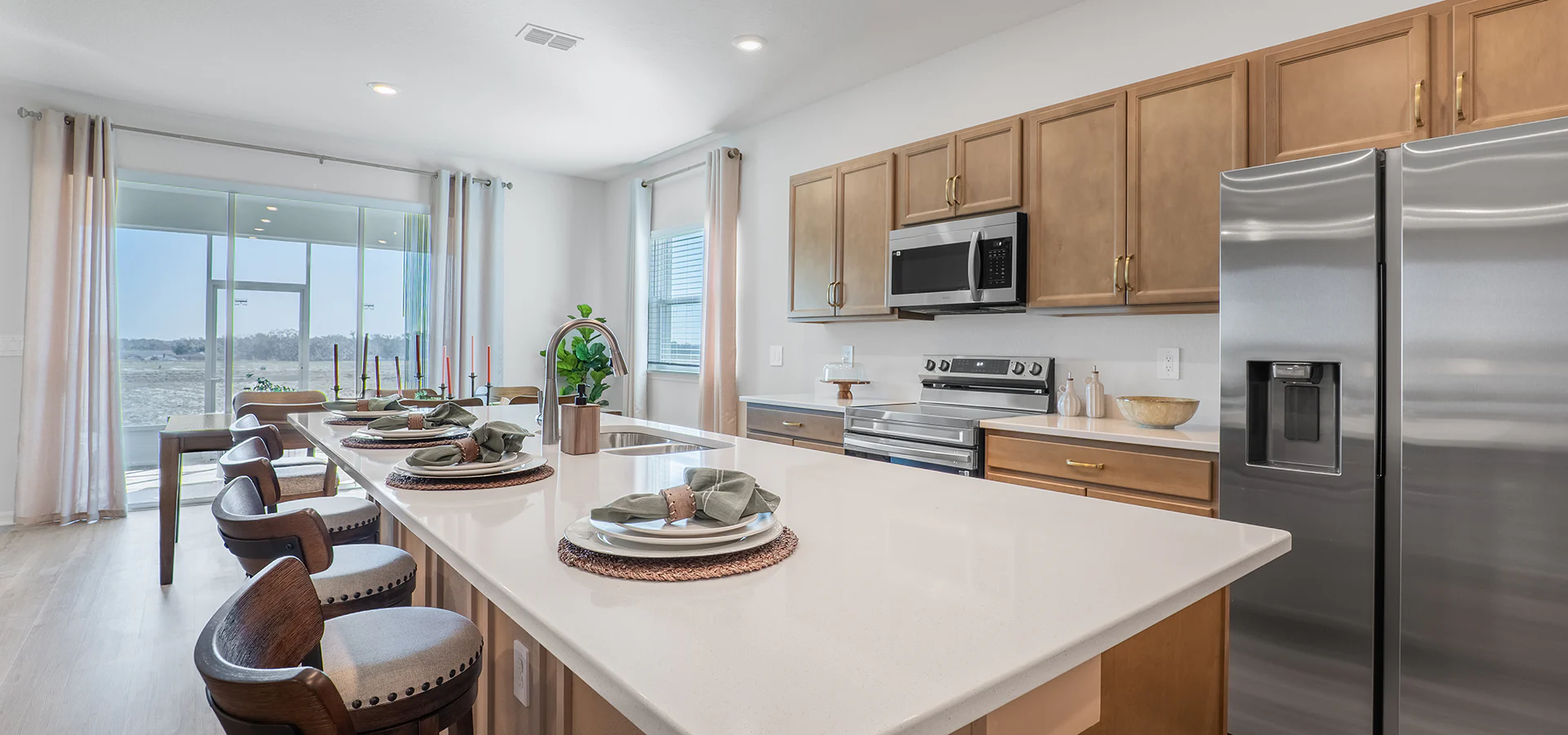 Sunny, open kitchen with wood cabinets, a large island with quartz and seating, and a dining table next to a large sliding glass door